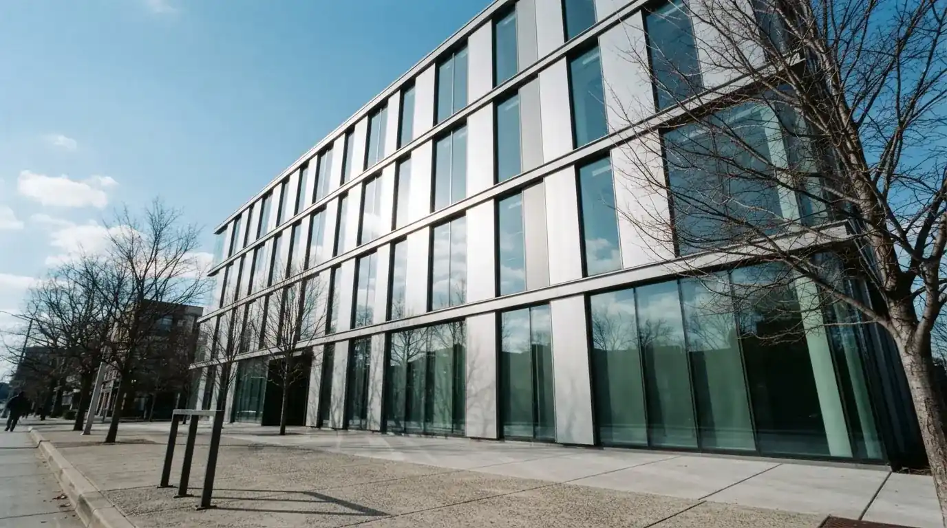 Edificio moderno de oficinas con grandes ventanales de cristal reflejando el cielo, visto desde una calle peatonal.
