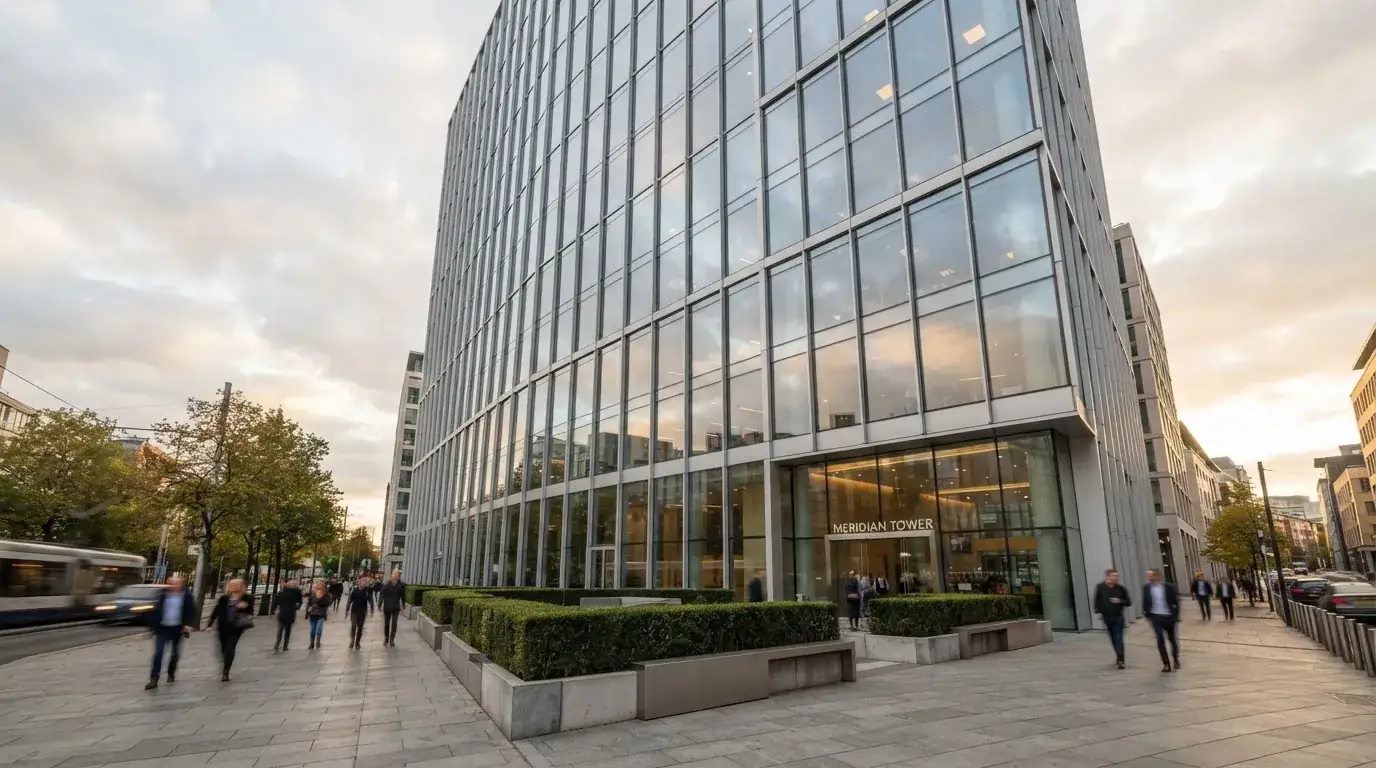 Un edificio de oficinas con fachada de cristal reflejando nubes, fotografiado desde una acera ancha por la tarde.